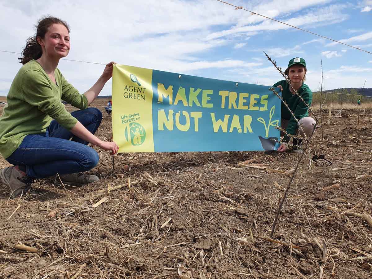 Bild: zwei Frauen mit Banner "make trees not war" auf der Aufforstungsfläche